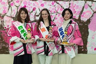 人形を手に持ち、タスキを掛けて桜の柄の法被を着た三人の女性の写真