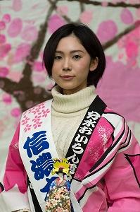 人形を手に持ち、タスキを掛けて桜の柄の法被を着たショートカットの女性の写真