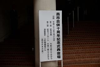 燕市文化会館入口前の白い柱に立てかけられた燕市合併十周年記念式典会場の文字と日時やスケジュールが書かれた白い看板の写真