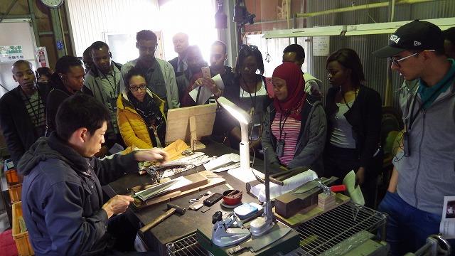 包丁づくりの様子を作業台に囲んで見学するアフリカ留学生達の写真