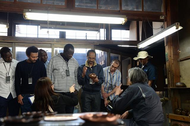 鎚起銅器の作品を実際に手にして観察するアフリカ留学生と説明を受けるアフリカ留学生達の写真