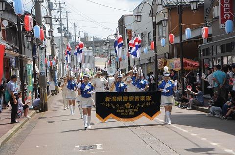 「新潟県警察音楽隊」の横断幕を持ち行進するコスチュームを着た女性たちの写真