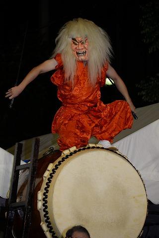 大きな和太鼓の上に乗るお面をつけた男性の写真