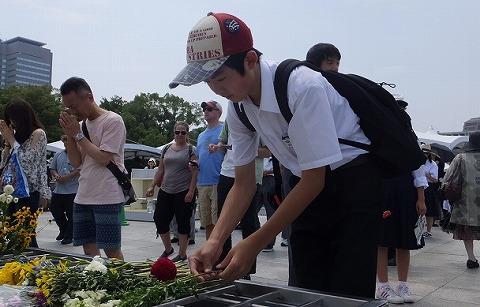 平和記念式典会場で原爆死没者慰霊碑に花を供える野球帽を被り黒いリュックを背負った男性生徒の写真