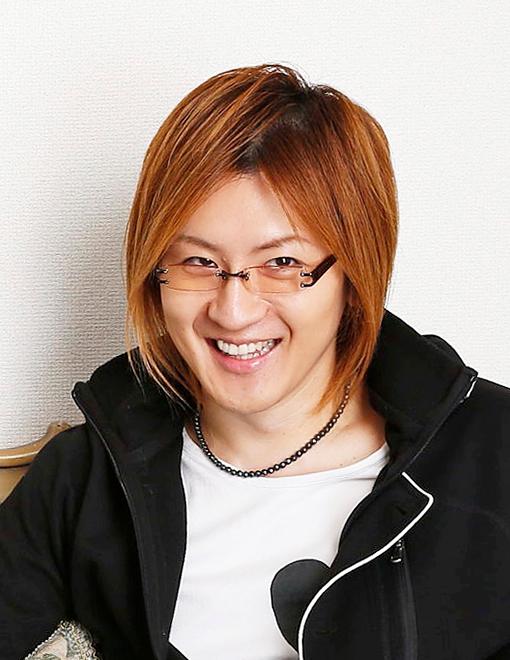 笑顔で眼鏡をかけて黒い上着の下に白い服を着た若新 雄純さんの顔写真