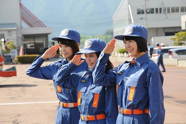 消防士の格好をして笑顔で敬礼をする3人の女性の写真