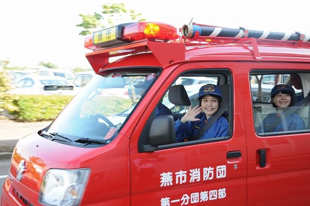 消防車から、笑顔を向ける消防士の服装をした女性たちの写真