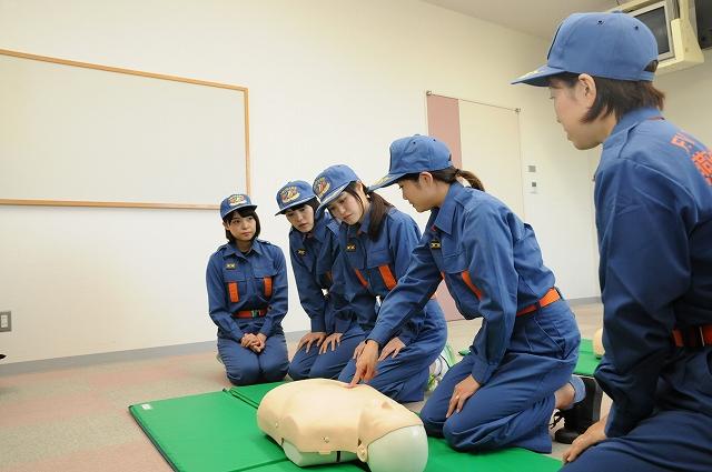 心臓マッサージ用の人形を前に応急手当の練習をする消防士の服装をした女性たちの写真
