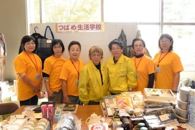 ホワイトボードの前の前に並ぶオレンジのTシャツや、黄色いジャンパーを着た7人の女性の写真