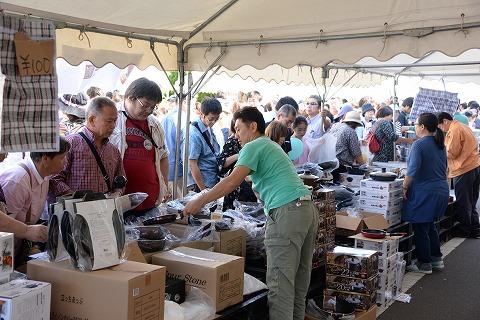 テントの下で調理器具を売る人たちと、見物する客の写真