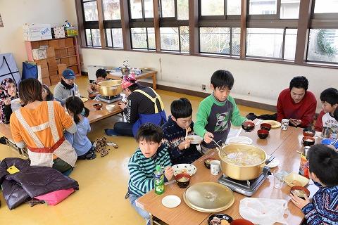 大人と子供たちが、それぞれの長机を囲んで豚汁とお餅を食べている写真
