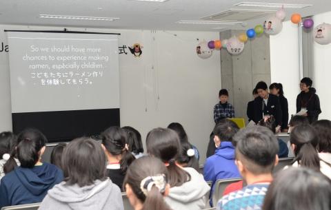 前に立ちスクリーンに成果発表を写し話す中学生の子たちと座って聞く受講生の子どもたちの写真