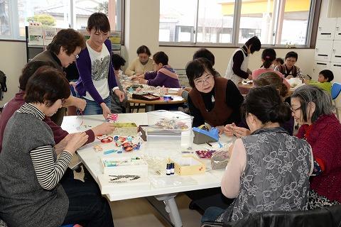 工作用の材料が並べられた白いテーブルを囲んで各々手を動かす高齢女性たちの写真