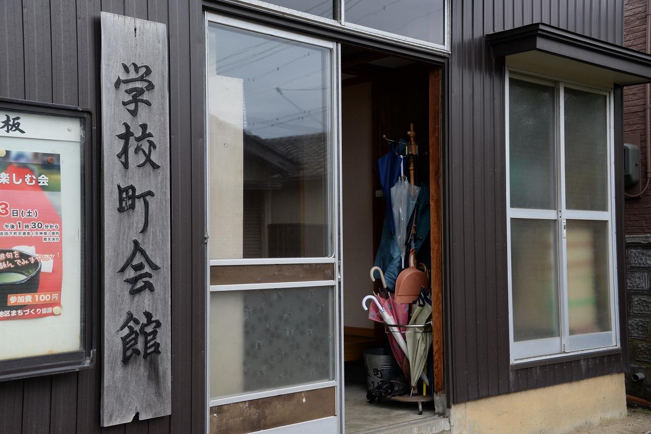 傘立てと看板がある吉田学校町会館入口の写真