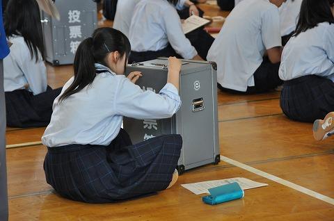 あぐらをかいて投票箱に触ってみている女子高校生の写真