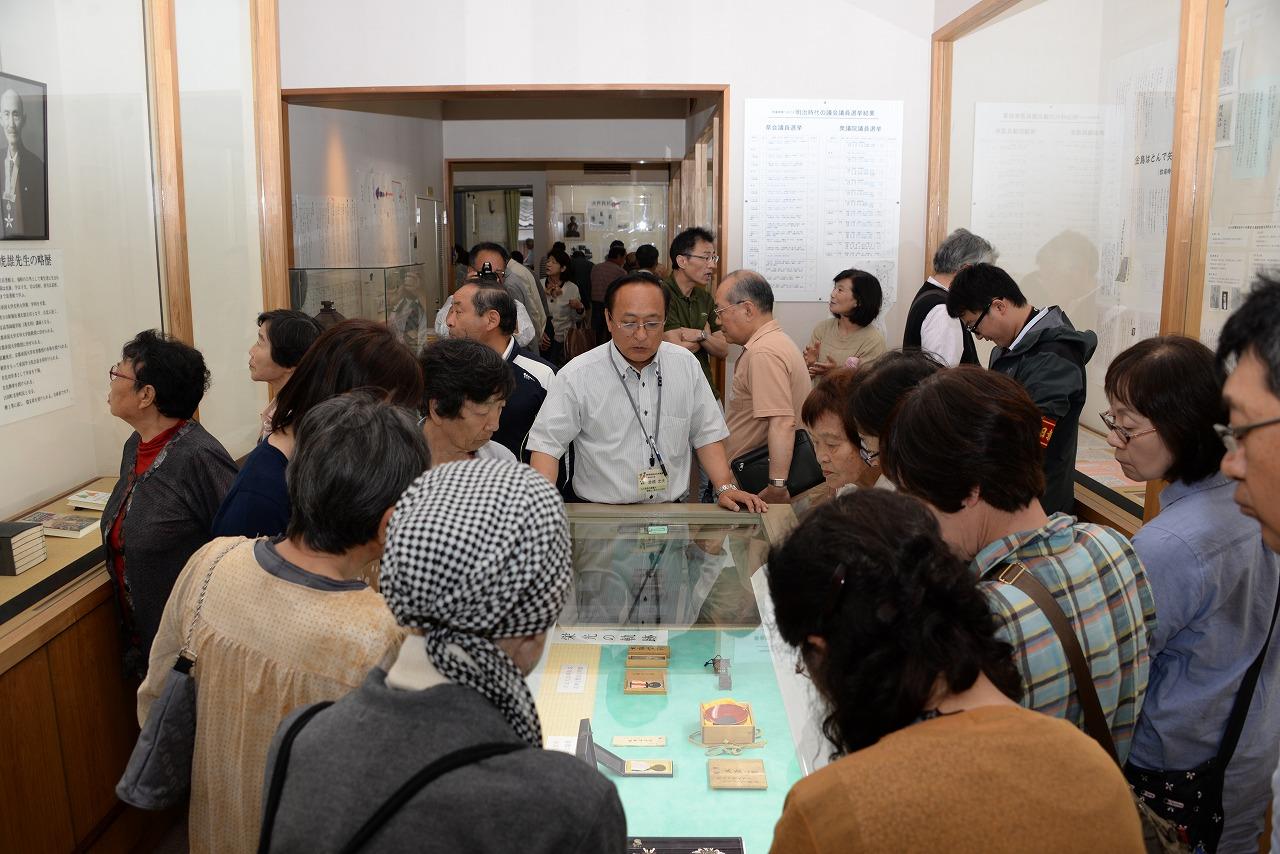 「史料館」の館内に展示物を解説している倉橋館長と展示物鑑賞する参加者たちの写真