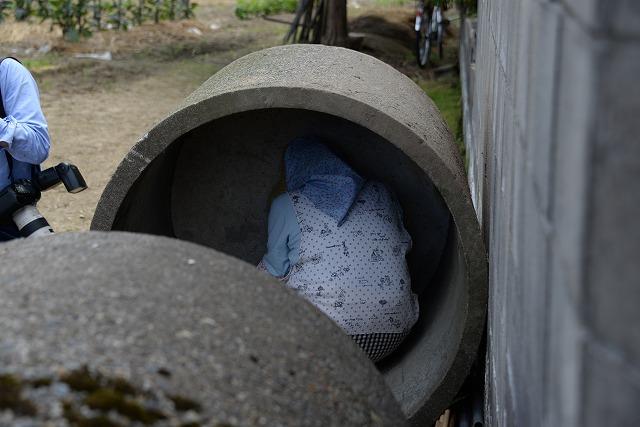 防災サイレンの鳴る中、人が入るくらいの大きい土管の中に避難する女性住民の写真