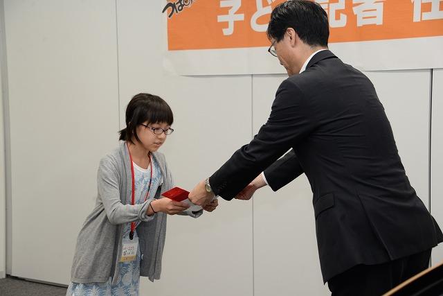 市長から記者の任命書と腕章を手渡されているグレーのカーディガンを着た女の子の写真