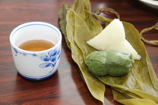 笹の葉の上に置かれた、緑色の団子と三角形のちまき、茶碗に入れられたお茶の写真