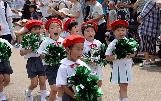 緑色の花飾りを持ってパレードに参加する子供たちの写真