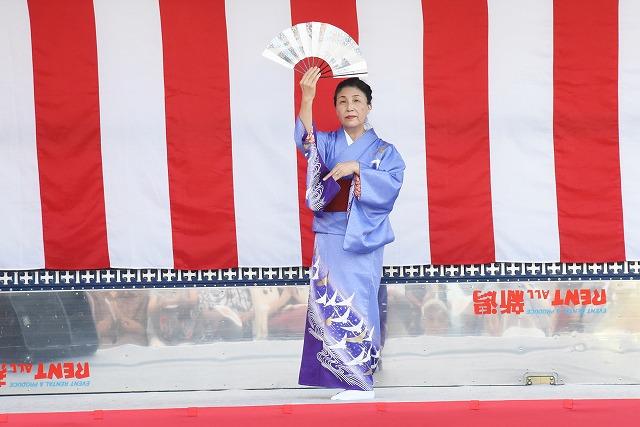 紫の着物をまとい、日本舞踊を踊っている年配の女性の写真