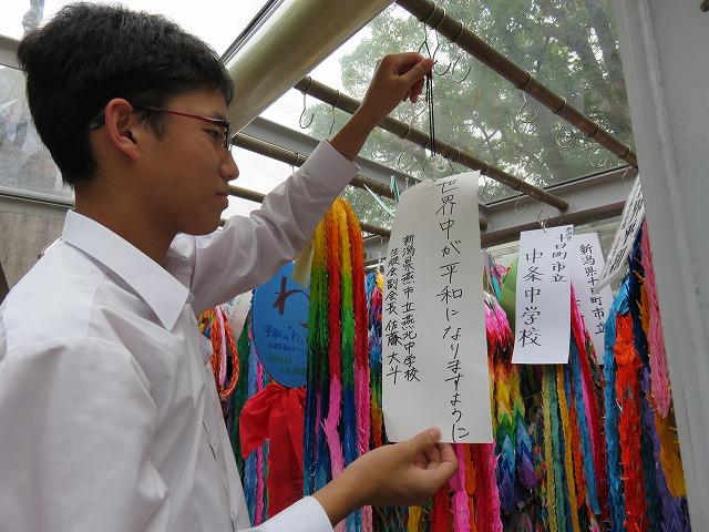 「世界中が平和でありますように」と書かれた短冊と千羽鶴を奉納する奉納する男子生徒の写真
