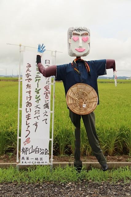 柳山自治会による「男性」の案山子と「災害に備えて、コミュニケーションが大切」と書かれたのぼりのの写真
