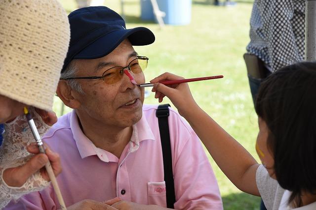 赤い絵の具がついた筆で、鼻をメイクされている笑顔のおじいちゃんの写真