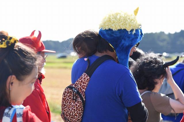 行列の中で子供を抱っこしながら歩いている、青い服を着て青い被り物をした鬼の仮装をした男性の写真