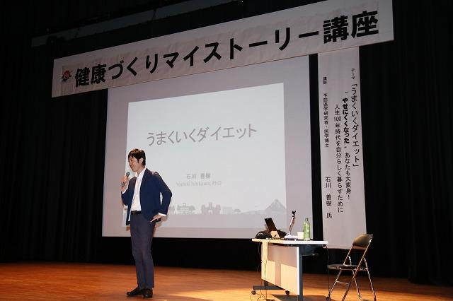 スライドの前でマイクを持って自己紹介をする石川善樹先生の写真