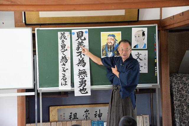 黒板に貼られた漢詩を解説する袴姿の男性の写真