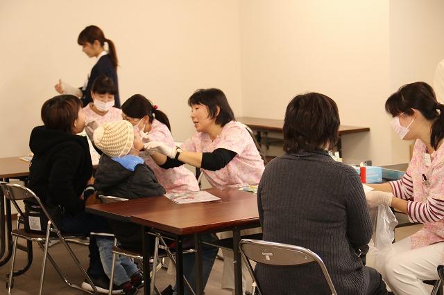 歯の様子を検診しているピンクの服を着た女性看護師たちに検診してもらっている参加者たちの写真