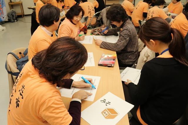 細長いテーブルで、用紙に覆いかぶさるようにして色付きのペンで書き込んでいる参加者や、座って眺めている参加者の写真