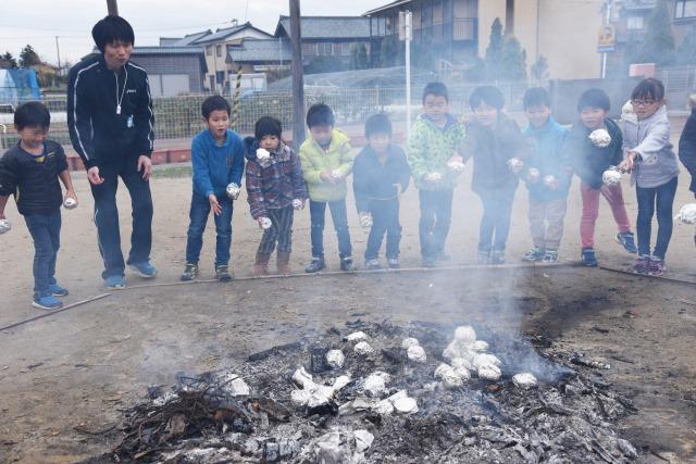 9人の子ども達と2人の大人がアルミホイルに包んださつまいもを火の中に投げ込んでいる様子の写真