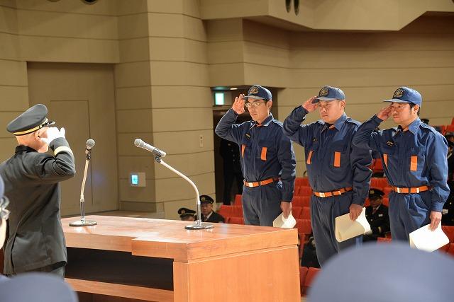 壇上で表彰状を持ち消防職員に敬礼をする3人の消防団員の写真