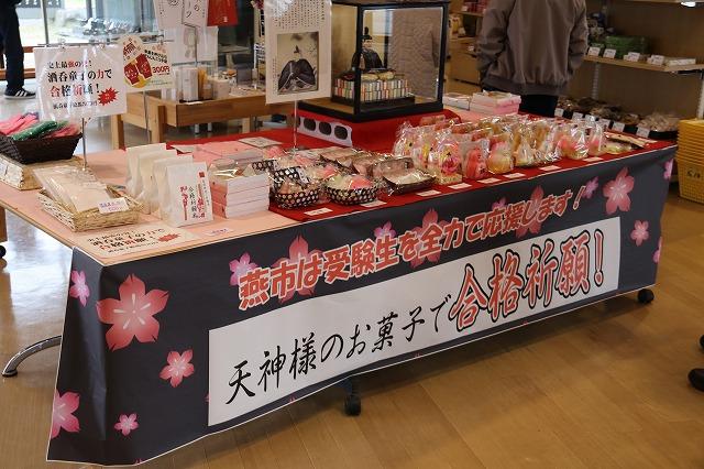 赤いテーブル上の透明箱にある「菅原道真公」の人形と陳列された色鮮やかな3種類の「天神講菓子」の写真