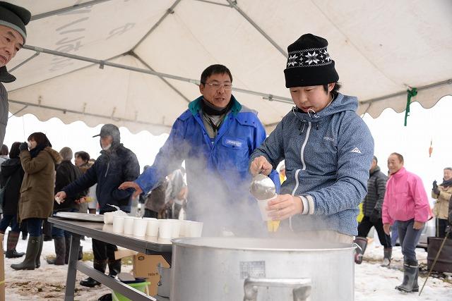 仮設テント内で大きい鍋に入った甘酒を紙コップに注ぎ並べる男性参加者たちの写真
