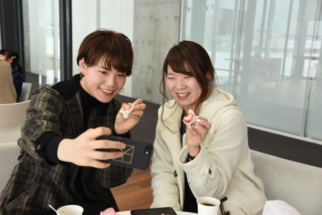 いちご大福を手にスマートフォンで写真を撮っている2人の女性の写真