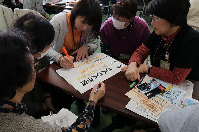 プロジェクト「わくわく手芸」の内容を紙に書き込むオレンジ色シャツを着た職員と打ち合わせをする参加者たちの写真
