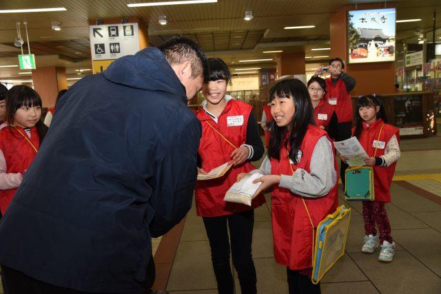 駅で東京方面から来た新幹線のお客さんに分北米をPRする小学生たちの写真