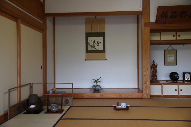 掛け軸と生け花が飾られ、角に茶道の道具が置かれた和室の写真