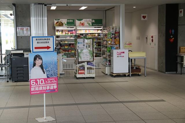 施設内の小さな売店の前に、「新潟知事選挙 期日前投票所」と書かれた立て看板が置かれている写真