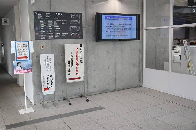 液晶画面と施設の案内が掲示された壁の前に、「期日前投票所」の立て看板が置かれている写真