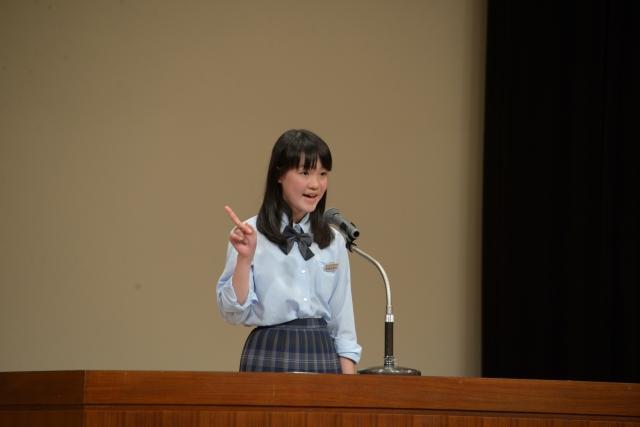 右手のひとさし指を立ててスピーチをしている制服姿の女子の写真