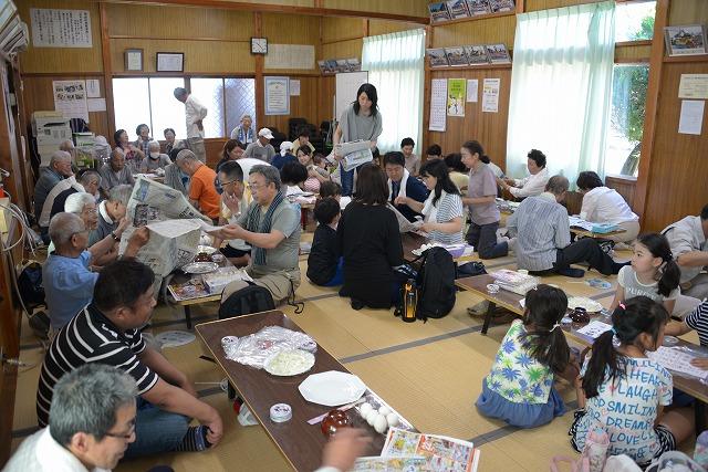 畳に並んだ長机に、住民がそれぞれ集まって座り、ごはんを食べたり新聞を読んだりしている写真
