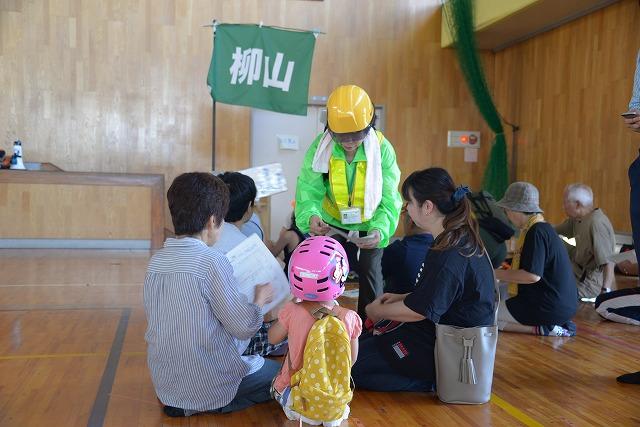 体育館で集まって座っている親子に、黄緑のジャンパーを着たスタッフが確認をとっている写真