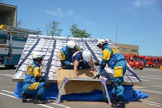 屋根の模型の上で、制服を着た人たちが被災者を助け起こそうとしている写真