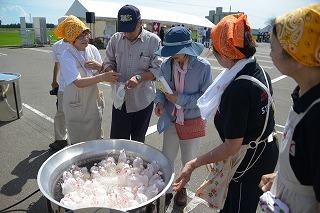 鍋の周りで、参加者に料理を手渡しているエプロン姿の人たちの写真