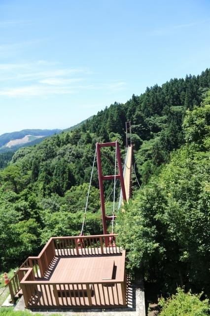 青空の下、木造の見晴台の奥につり橋がかかっている写真