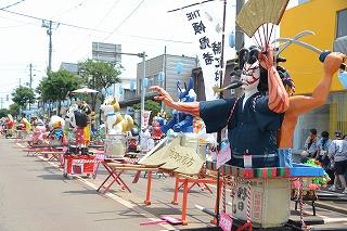 キャラクターや人物を模した形の神輿が、道の上にずらりと並んでいる写真